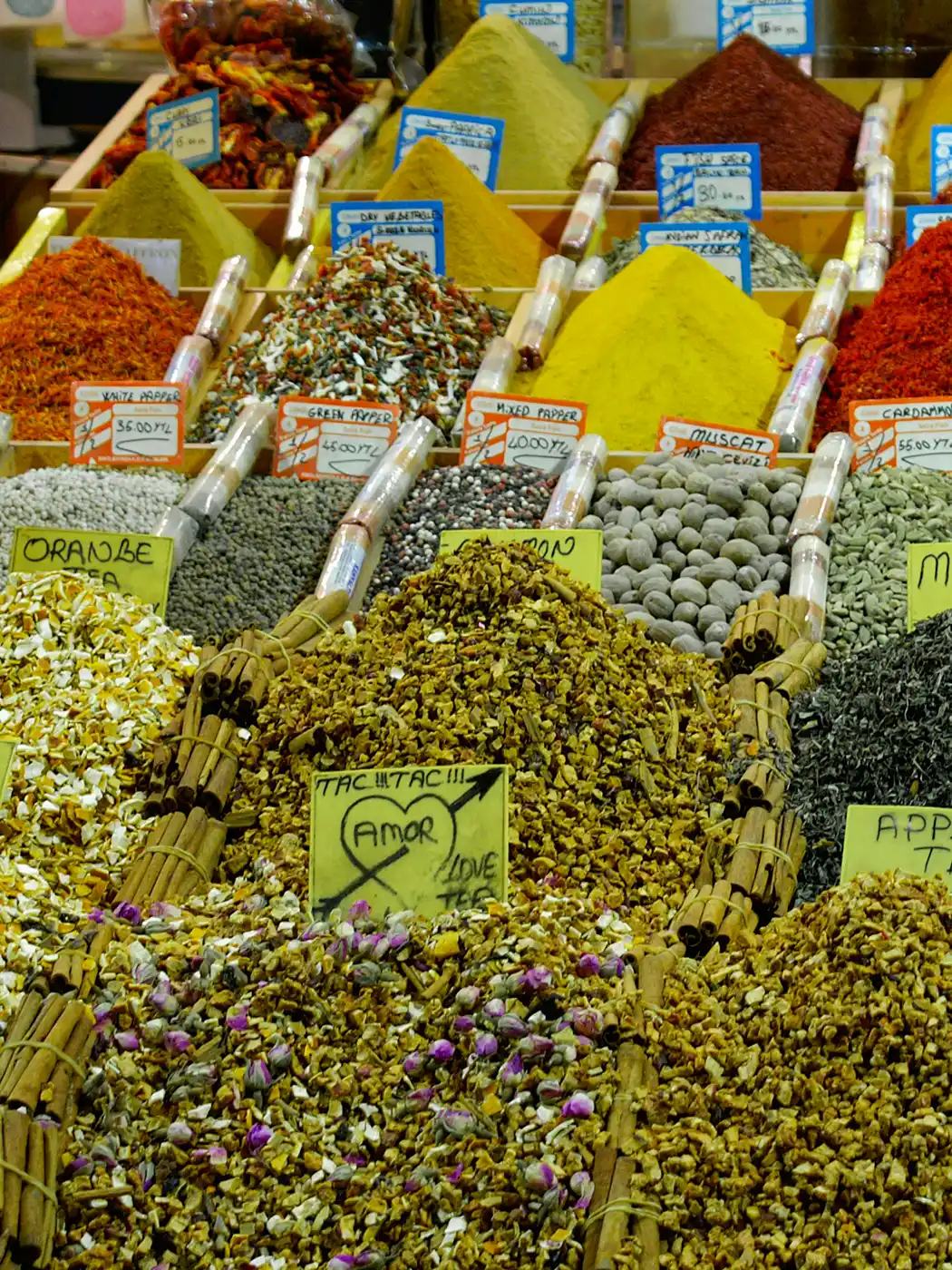 Istanbul-Gewuerzbasar-Tee Reihen von Gewürzen und getrockneten Kräutern in Behältern, die jeweils mit einem kleinen Schild beschriftet sind.