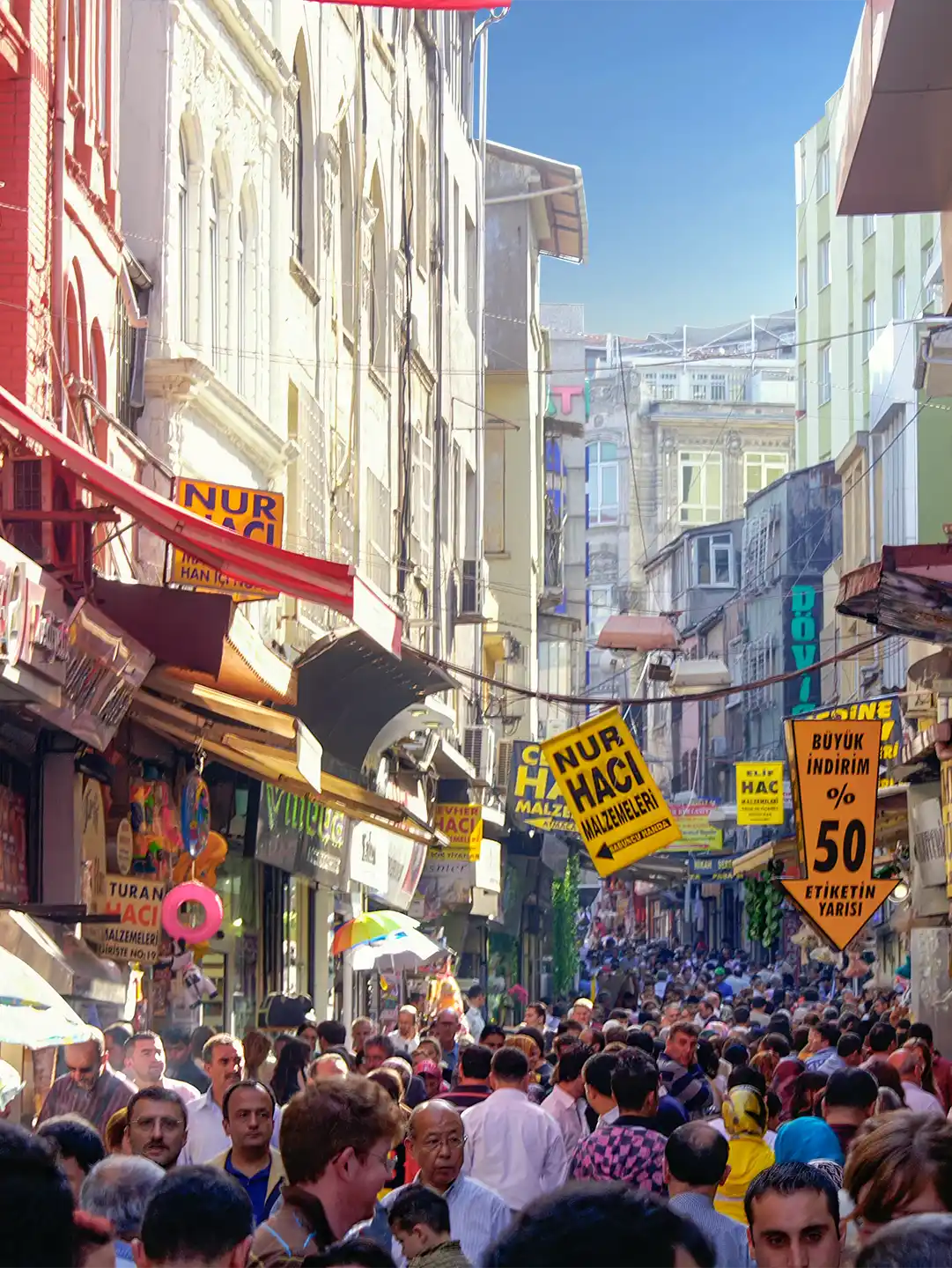 Istanbul-Gewuerzmarkt-Strasse Eine belebte, schmale Stadtstraße, gesäumt von hohen Gebäuden und hängenden Ladenschildern.