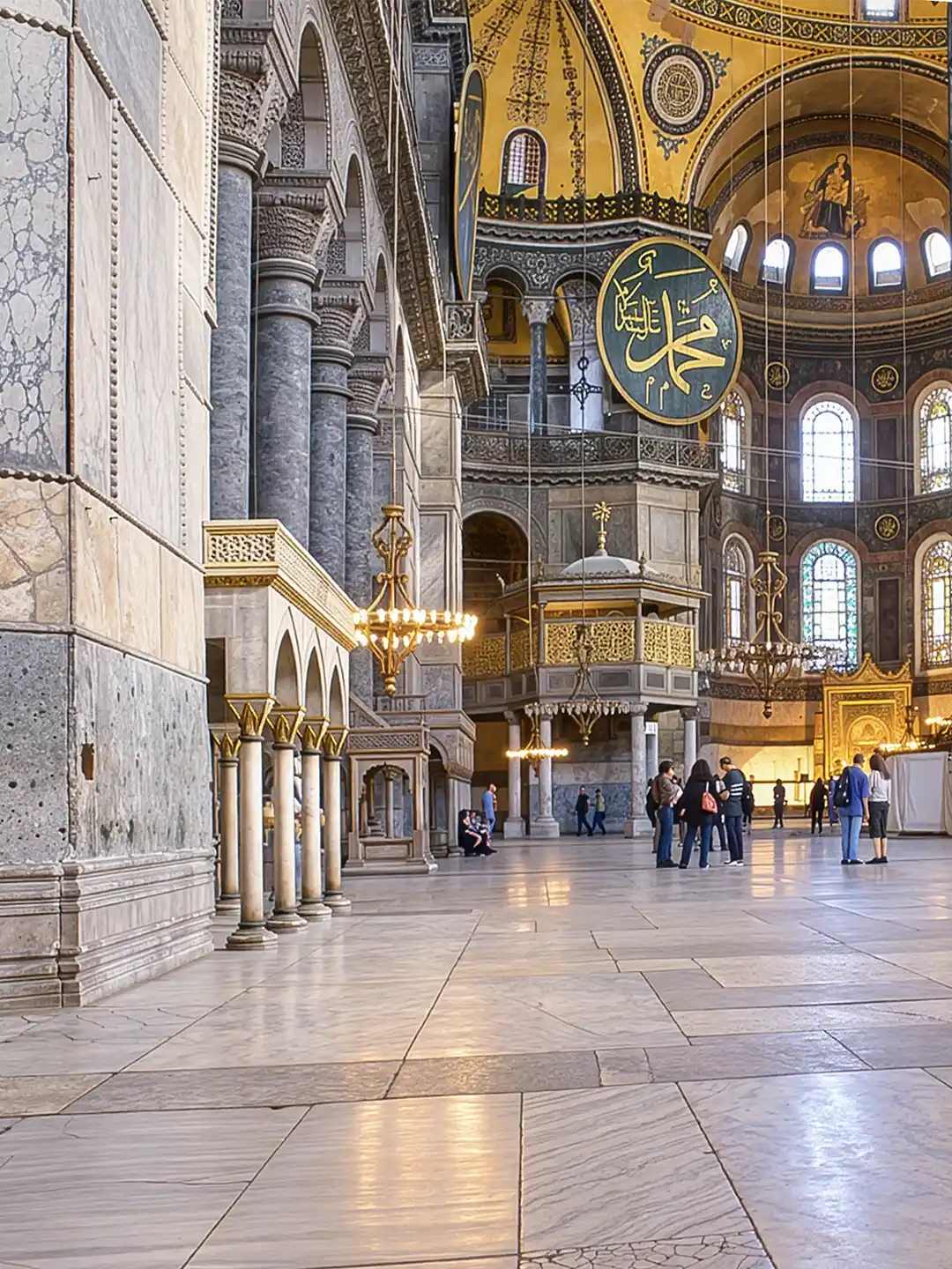 Istanbul-Hagia-Sophia-Marmor Innenansicht der Hagia Sophia mit Marmorsäulen, einer großen goldenen Kalligraphie-Scheibe und Besuchern in der großen Halle.