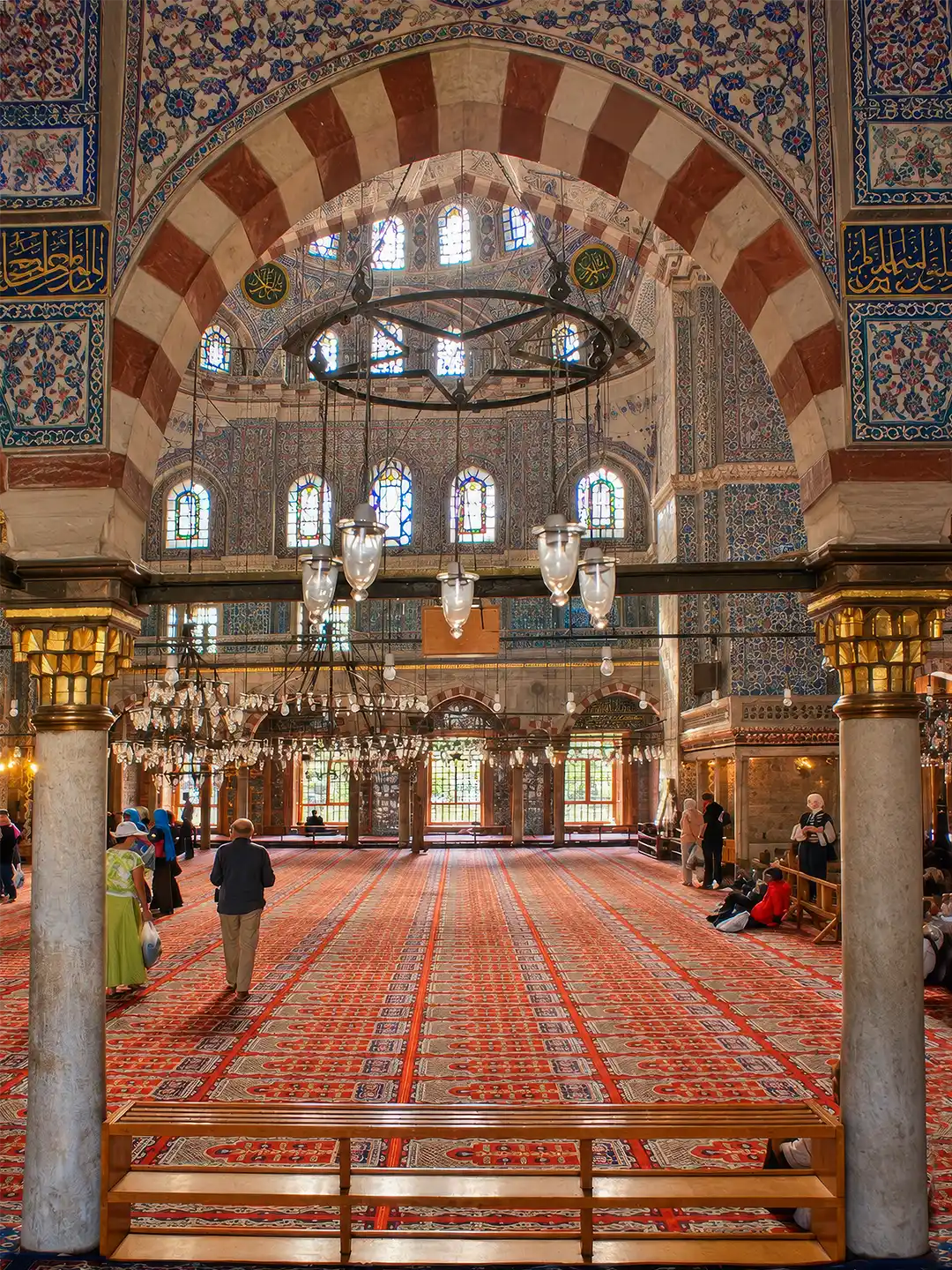 Istanbul-Sultan-Ahmed-Moschee Das Innere der Sultanahmed-Moschee mit gekachelten Wänden, kunstvollen Bögen und großen Kronleuchtern, die über einem roten Teppich hängen.