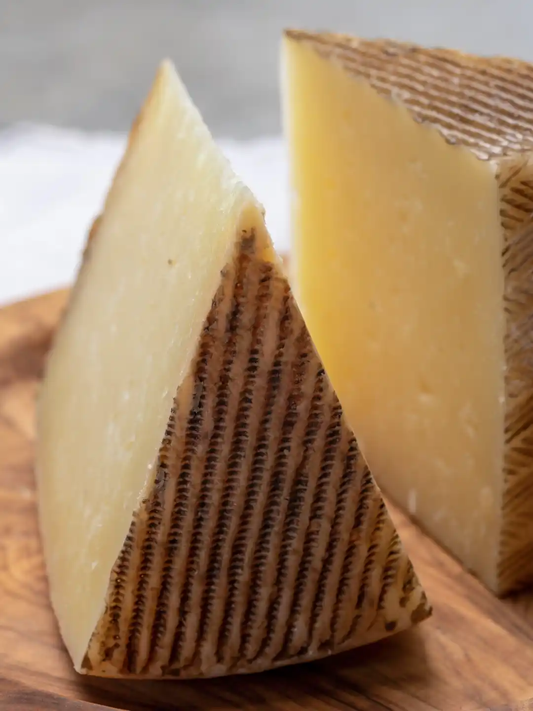 Zwei Stücke Hartkäse mit strukturierter brauner Rinde auf einem Holzbrett.