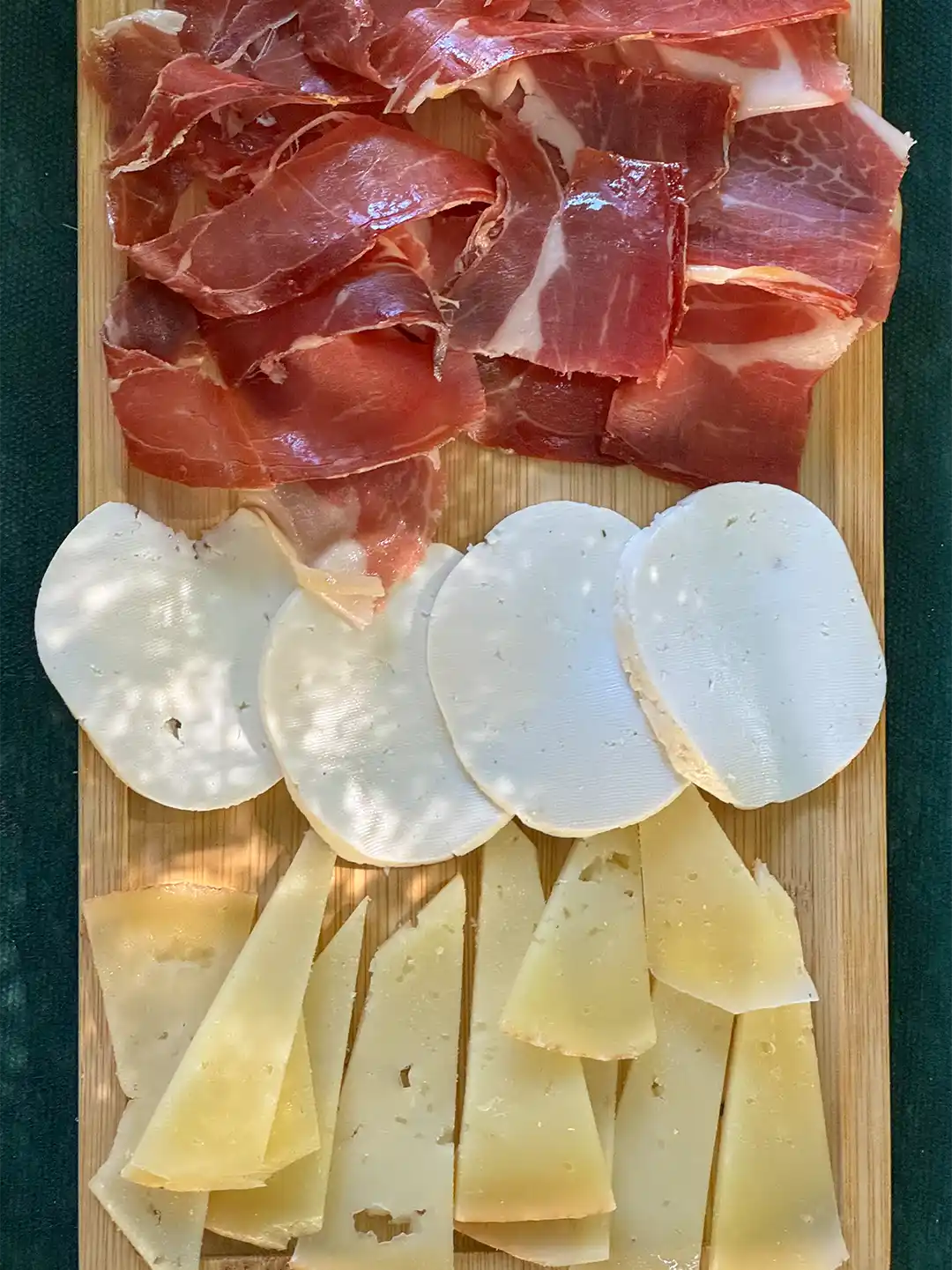 Ein Holzbrett, belegt mit Scheiben von geräuchertem Schinken, frischem Mozzarella und Hartkäse-Ecken.