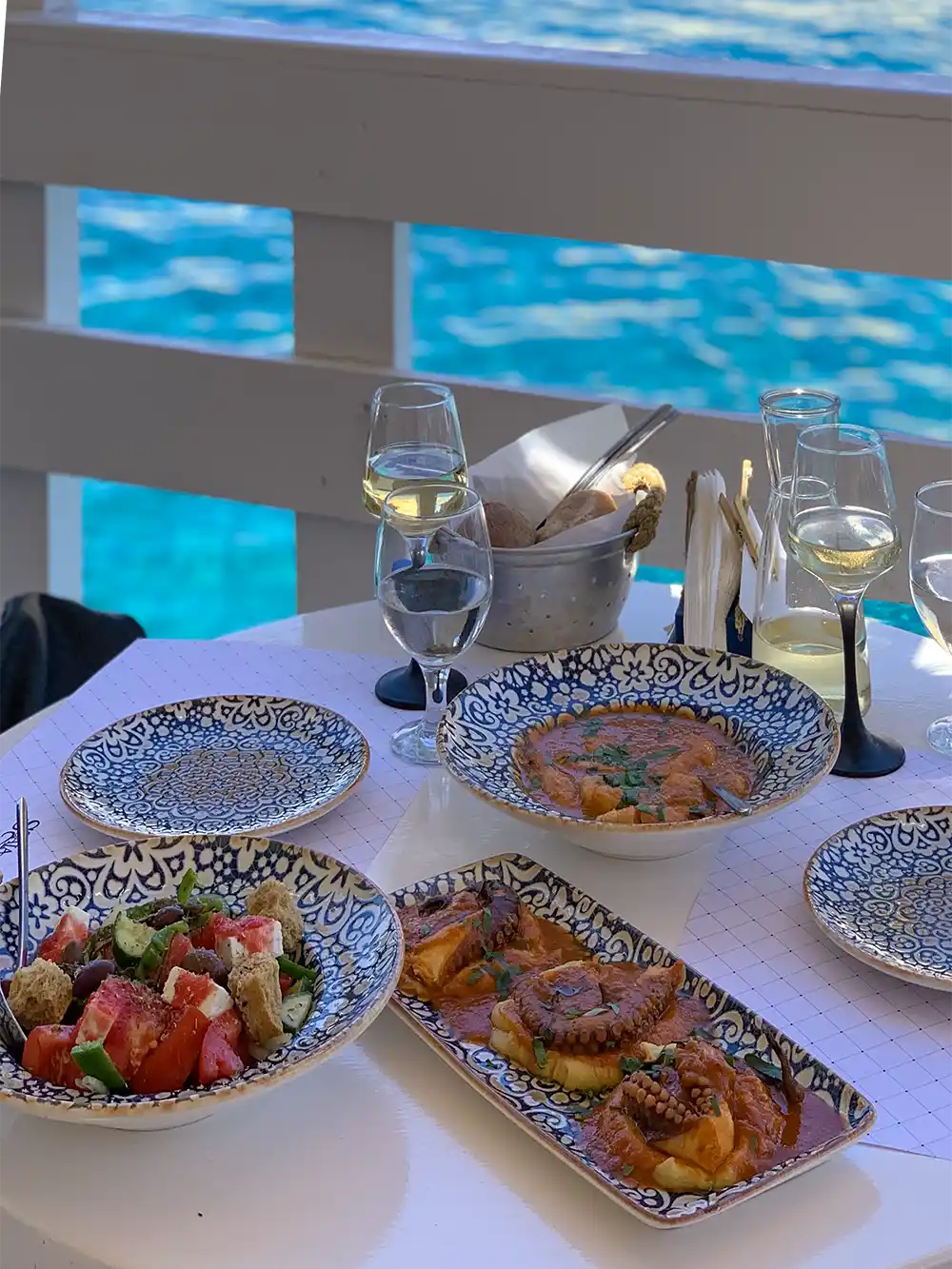 Griechischer Salat, Tintenfisch und Schüsseln mit Essen auf einem Restauranttisch mit Blick auf das Meer.