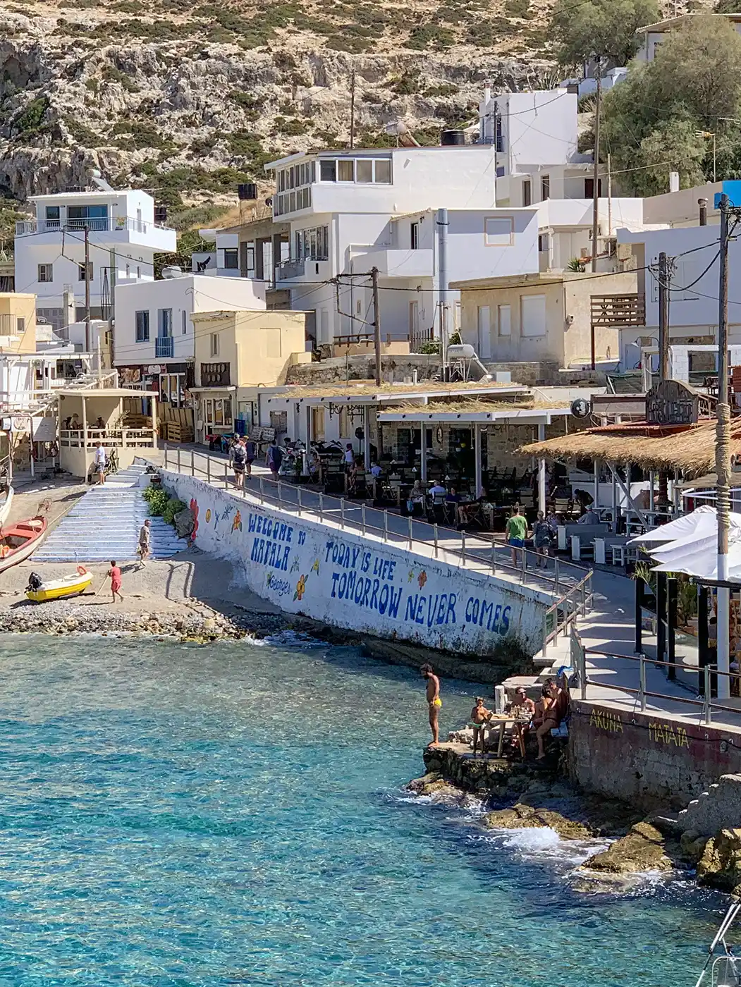 Matala-Spruch Dorf Matala am Meer mit weißen Gebäuden, einem Wandgemälde mit der Aufschrift "Heute ist das Leben, morgen kommt nie"