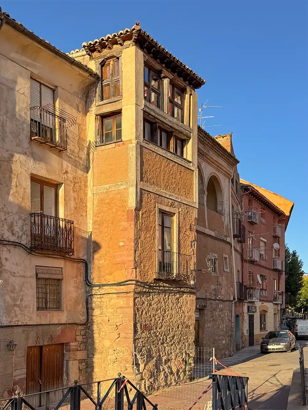 Molina-de-Aragon-Buergerhaeuser Alte, mehrstöckige Steinhäuser mit Balkonen, die entlang einer schmalen Straße unter einem strahlend blauen Himmel stehen.