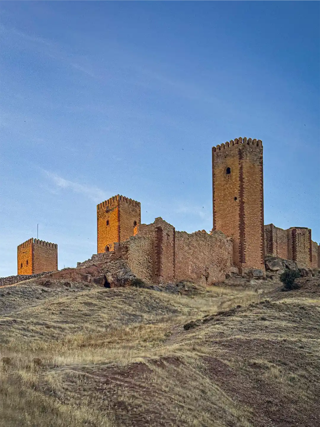 Molina-de-Aragon-Burgtuerme Ruinen einer Steinburg mit hohen Wehrtürmen auf einem grasbewachsenen Hügel.
