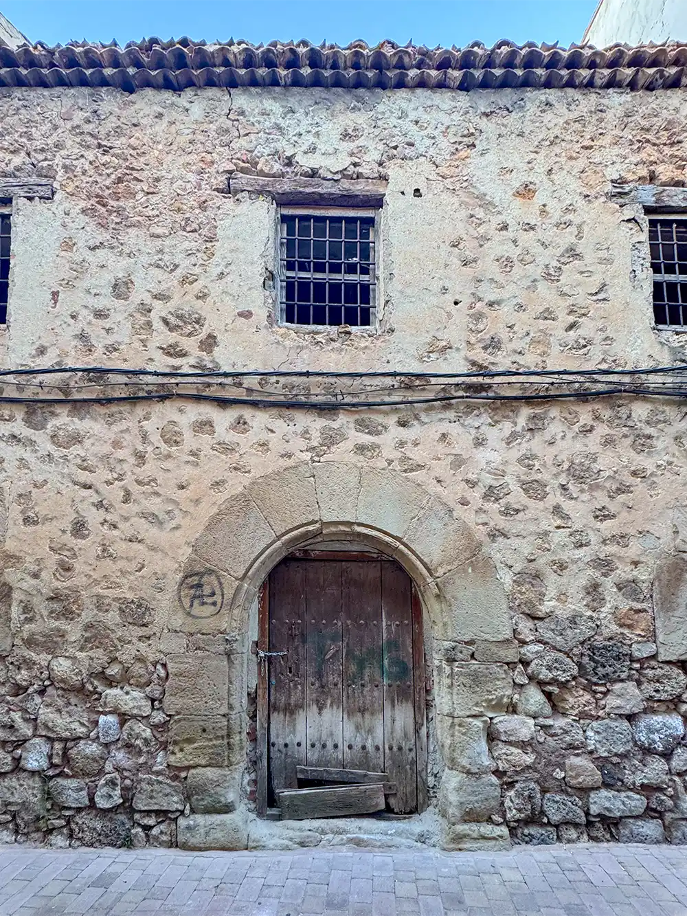 Molina-de-Aragon-Moraria-Viertel Altes Steingebäude mit einer Holztür, vergitterten Fenstern und einer kreisförmigen Markierung auf der rechten Seite.