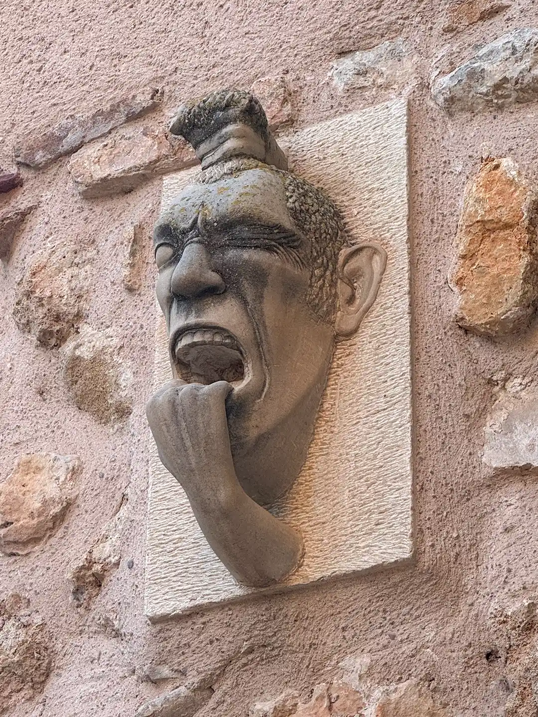 Molina-de-Aragon-Skulptur Steinwandrelief, das ein schreiendes Gesicht mit einer Hand im offenen Mund darstellt.