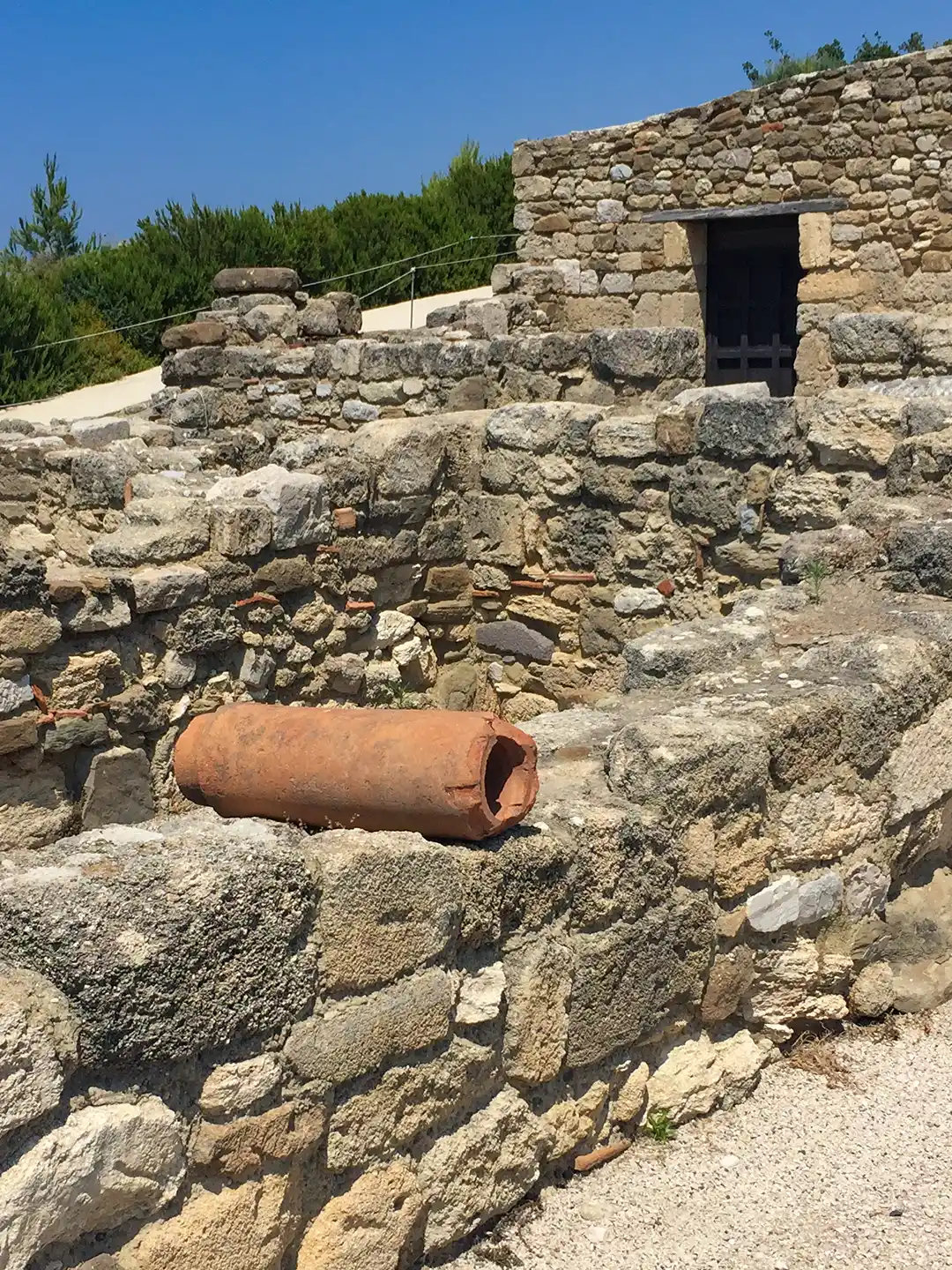 Rhodos-Kamiros-Tonroehre-Wasserleitung Ein Terrakotta-Rohrstück, das auf antiken Steinruinen ruht.