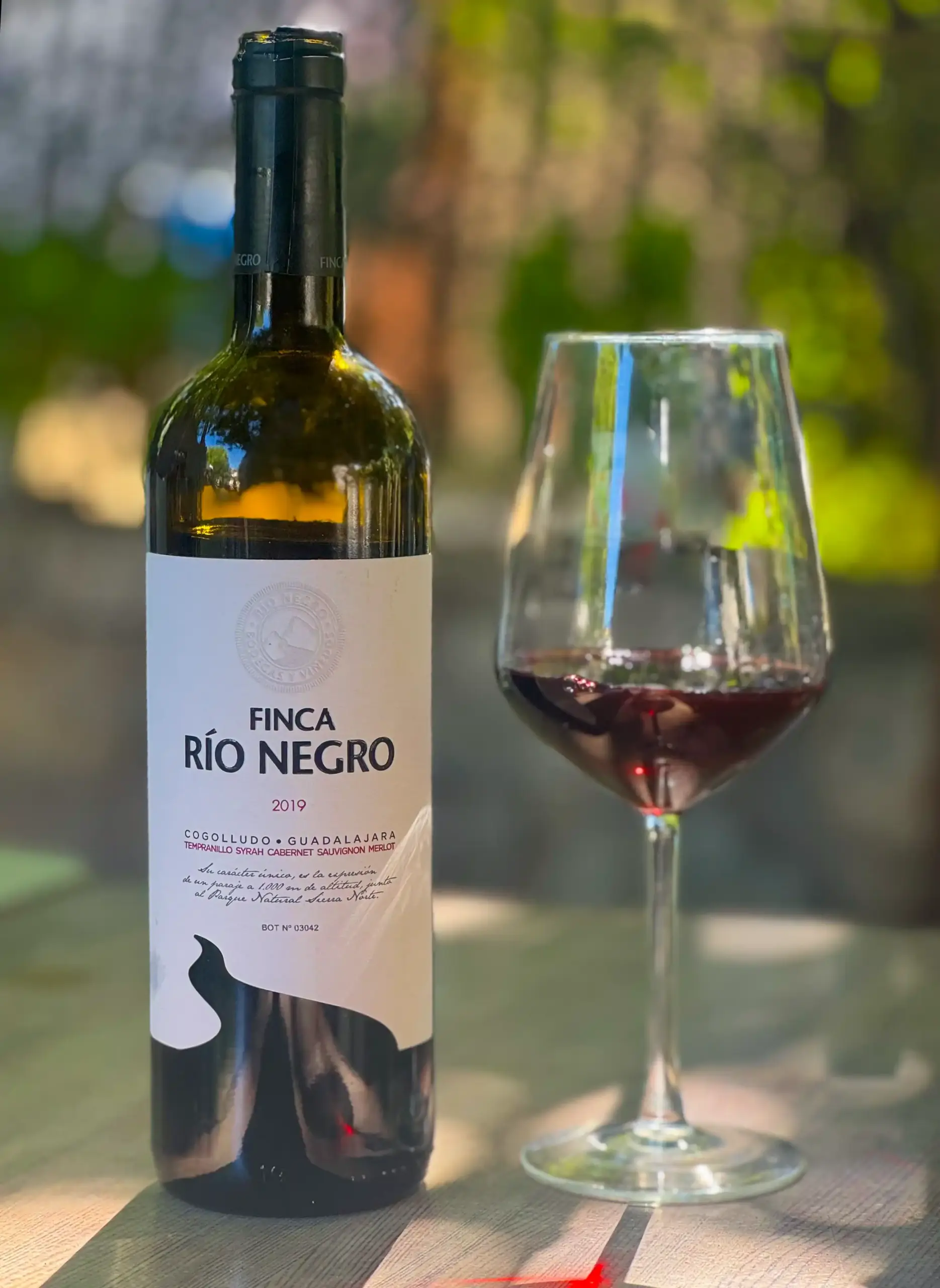 Eine Flasche Rotwein der Marke Finca Río Negro neben einem gefüllten Weinglas.