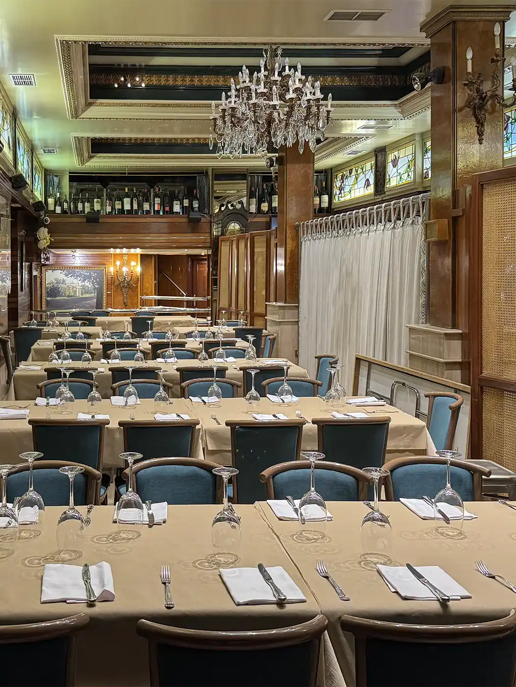 Ein Esszimmer, das für eine feierliche Veranstaltung hergerichtet ist, mit Tischreihen, blauen Stühlen und Kristallkronleuchtern.